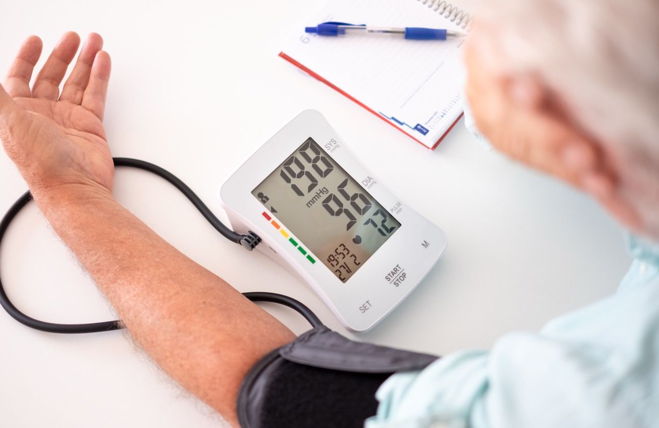Old senior man using medical device to measure blood pressure – elderly man suffering from hypertension sitting at home table taking care of his health Tensiómetro